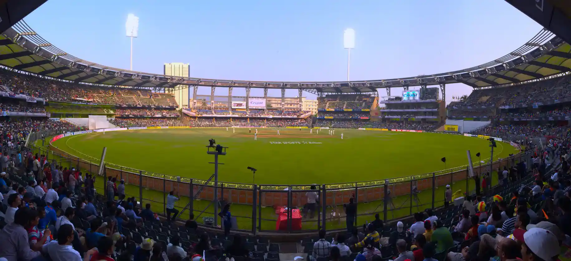 A photo of a large cricket stadium with green outfield, floodlights, and stands.